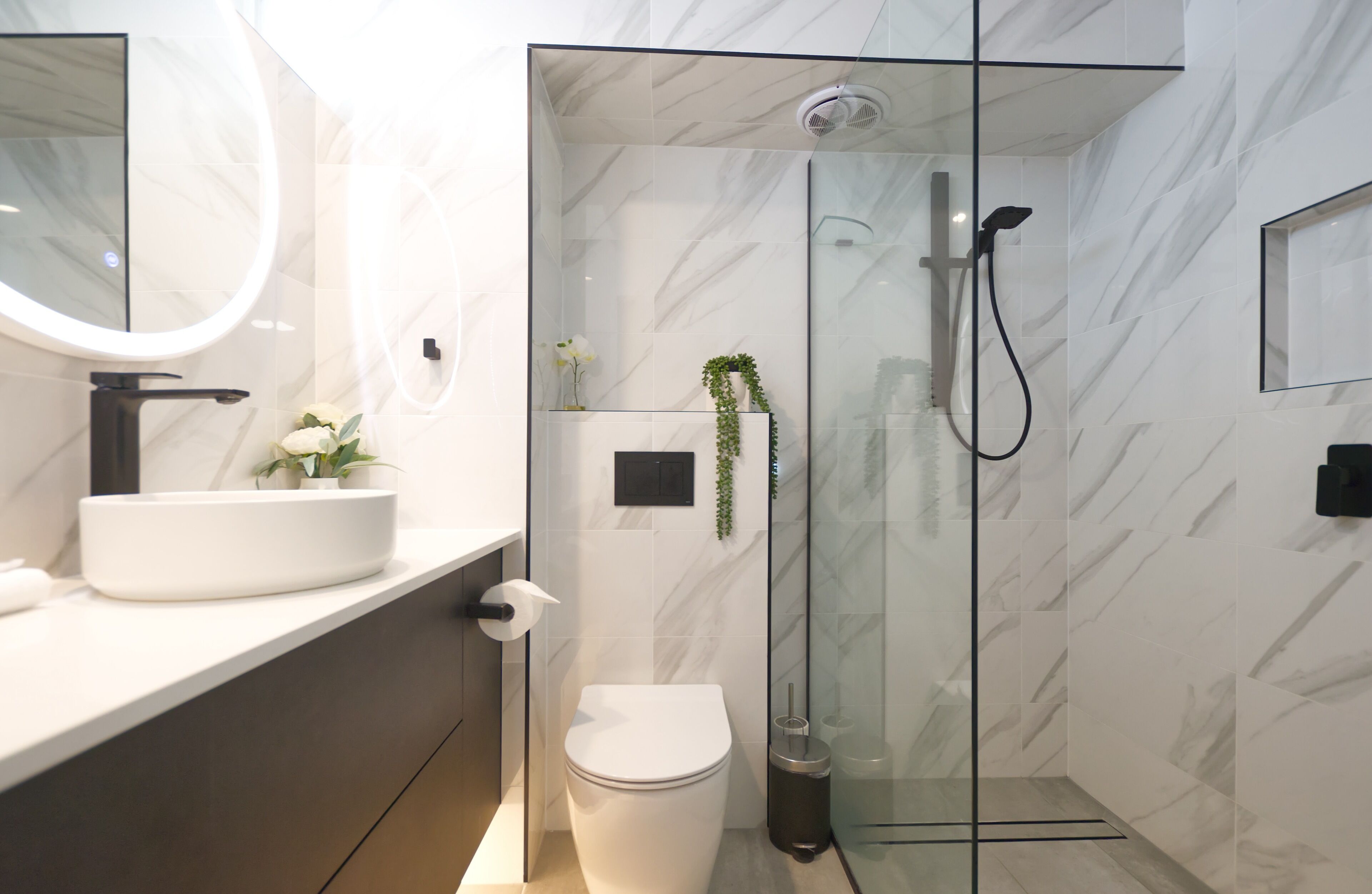 A modern bathroom with a glass-enclosed shower, a white toilet, and a marble-tiled vanity.