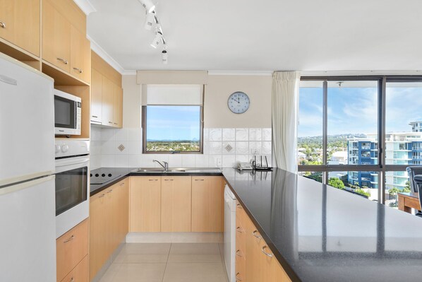 Una cocina moderna con armarios de madera, encimera negra y vistas a la ciudad a través de amplios ventanales.