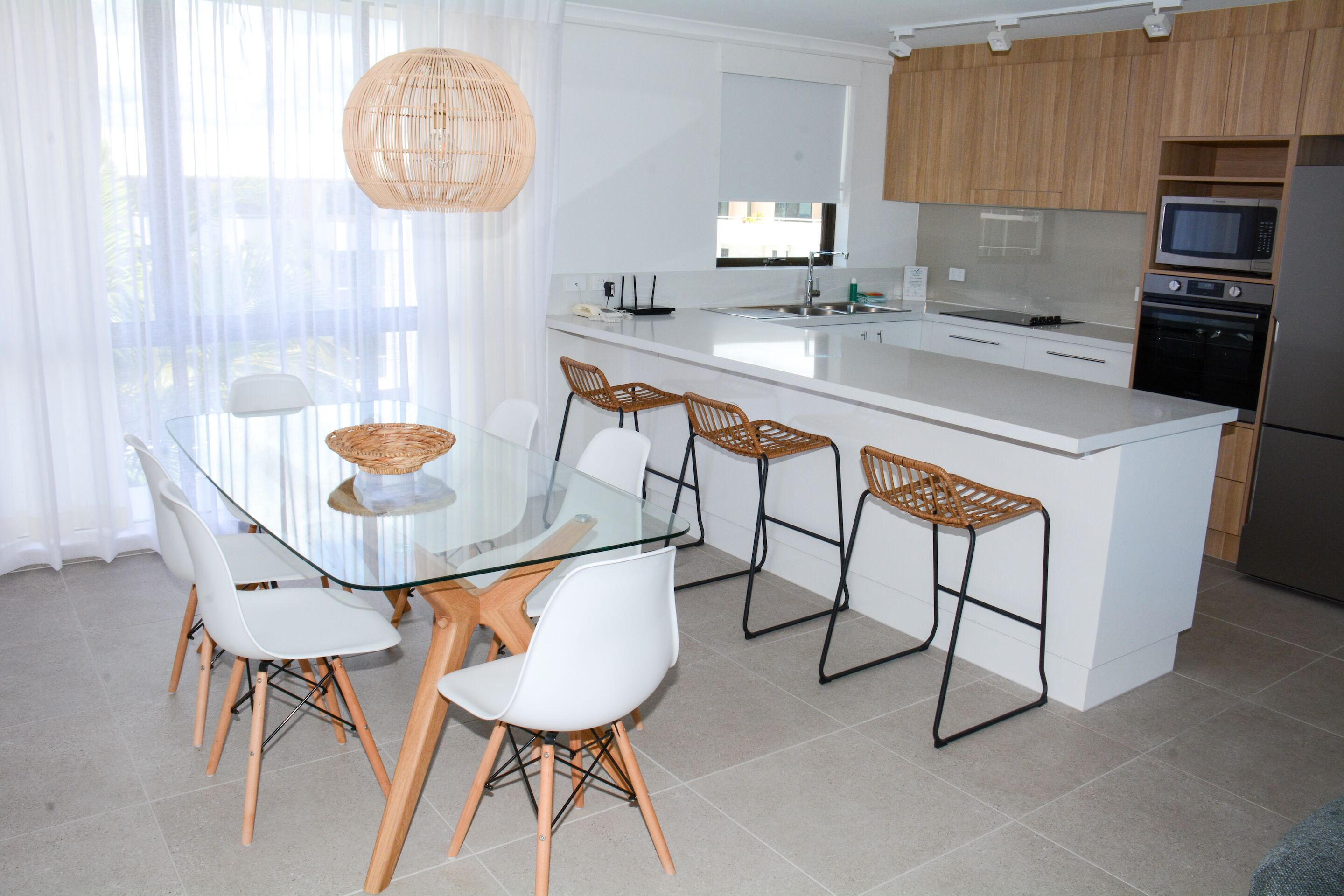 A modern kitchen with a large island, white cabinetry, and a dining area with glass table and white chairs.
