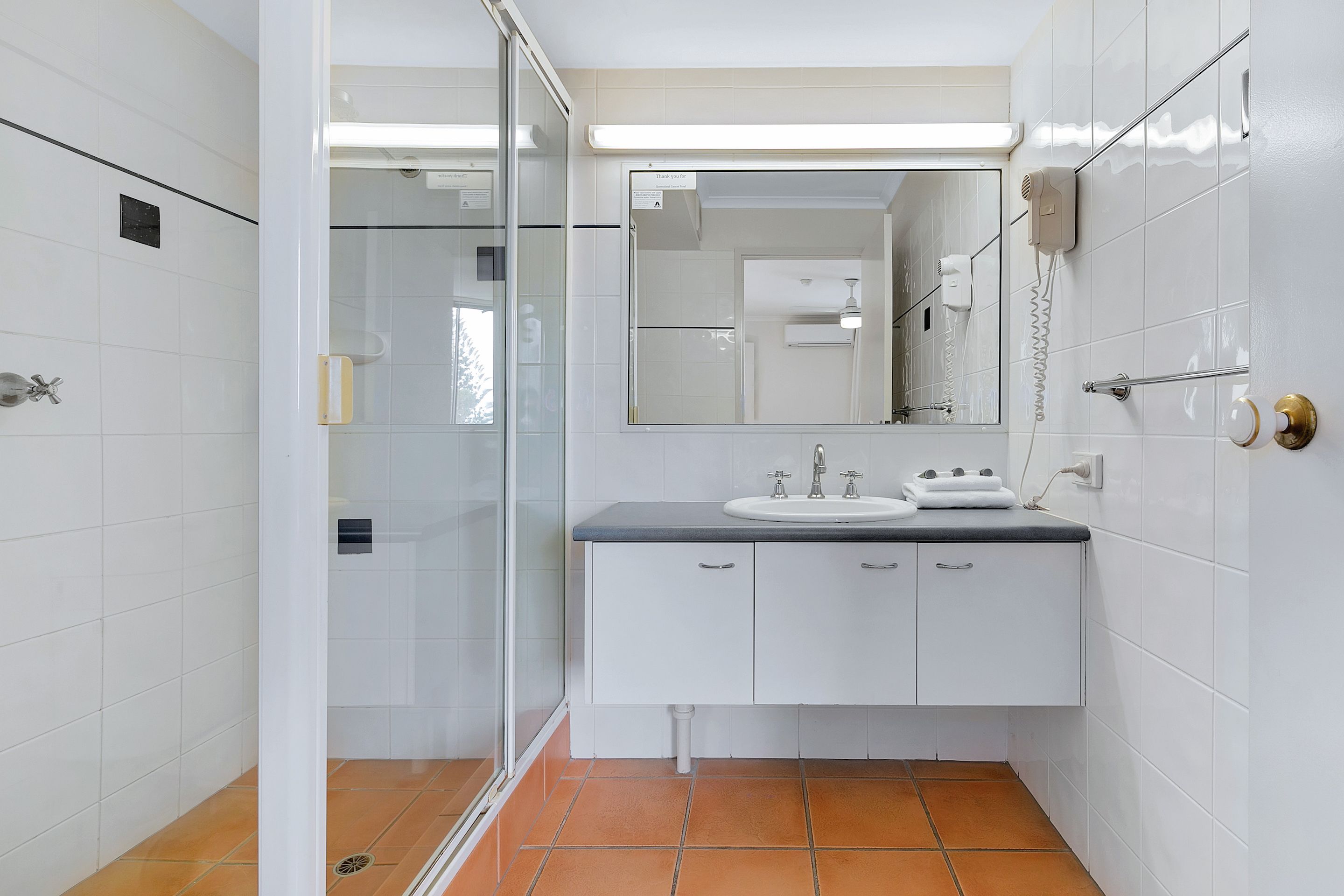 A bathroom with a glass shower enclosure, a white sink with a black countertop, and a mirror above the sink.