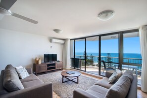 Una sala de estar con un sofá, una mesa de centro, un televisor y un balcón con vista al océano.