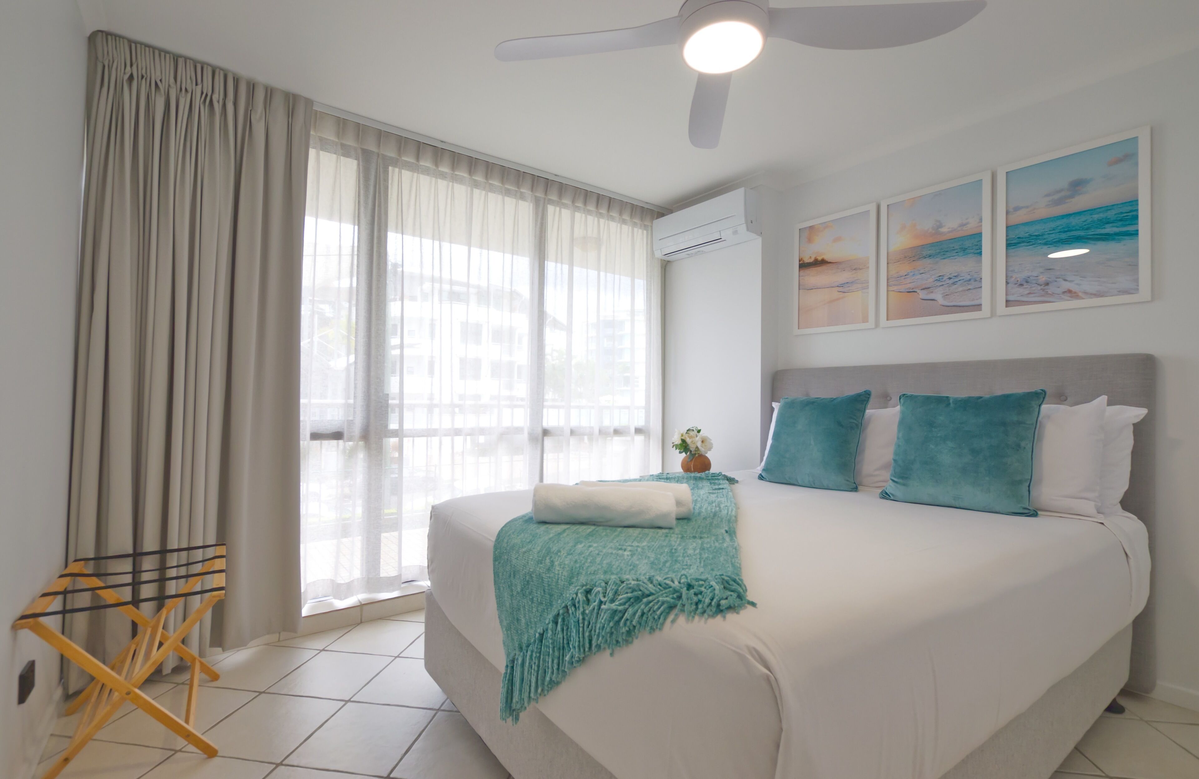 A bedroom with a large bed, a ceiling fan, and a window with sheer curtains.