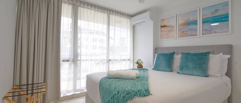 A bedroom with a large bed, a ceiling fan, and a window with sheer curtains.