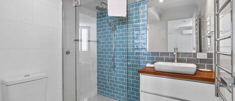 A modern bathroom with a glass shower enclosure, a white toilet, a sink with a wooden countertop, and a tiled backsplash.