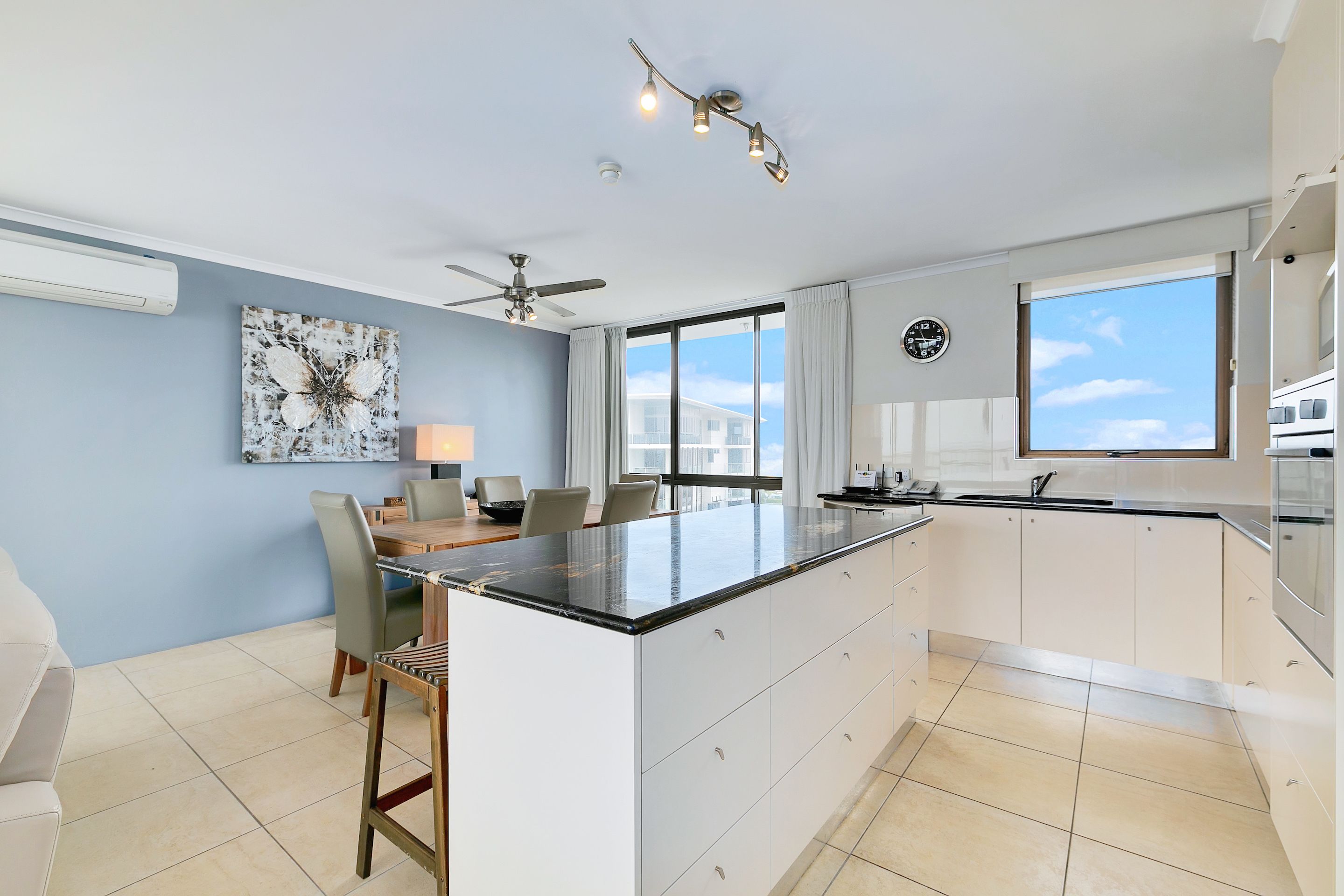 A modern kitchen with a large island, white cabinetry, and a ceiling fan.