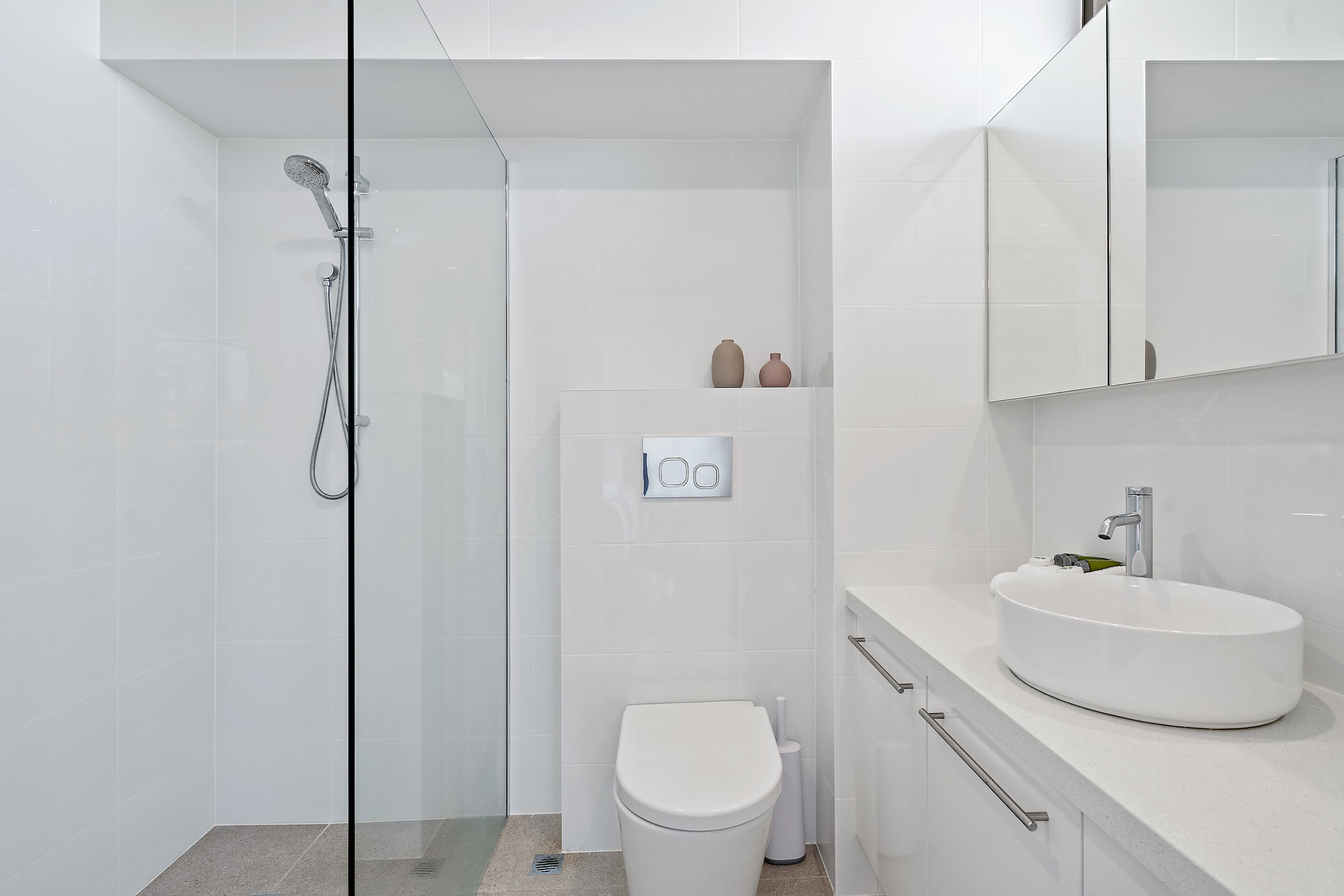 Une salle de bain moderne avec une douche à parois de verre, des toilettes blanches et un meuble-lavabo avec un évier et un miroir.
