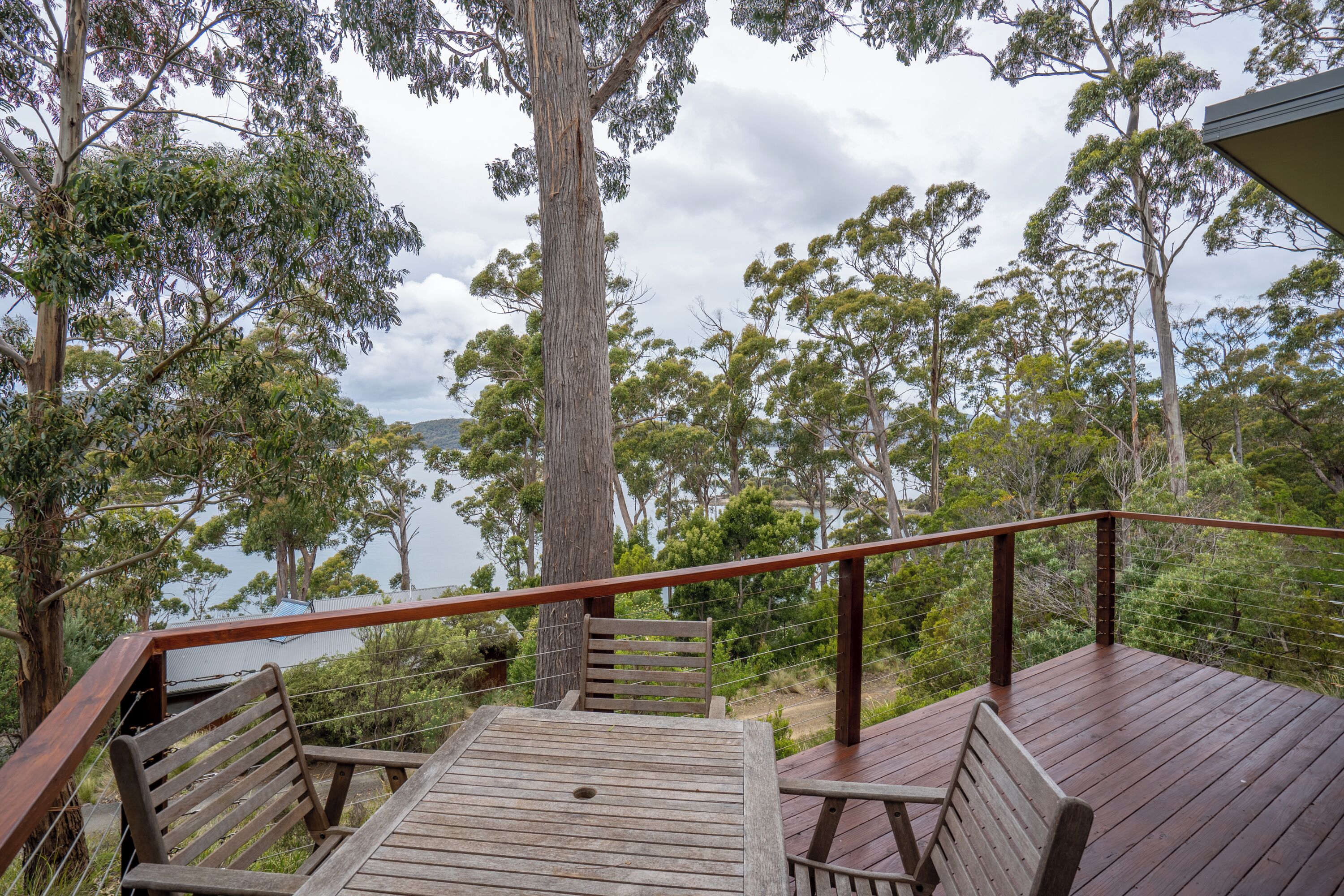 A wooden deck with a table and two chairs, overlooking a forested area with a view of the water.