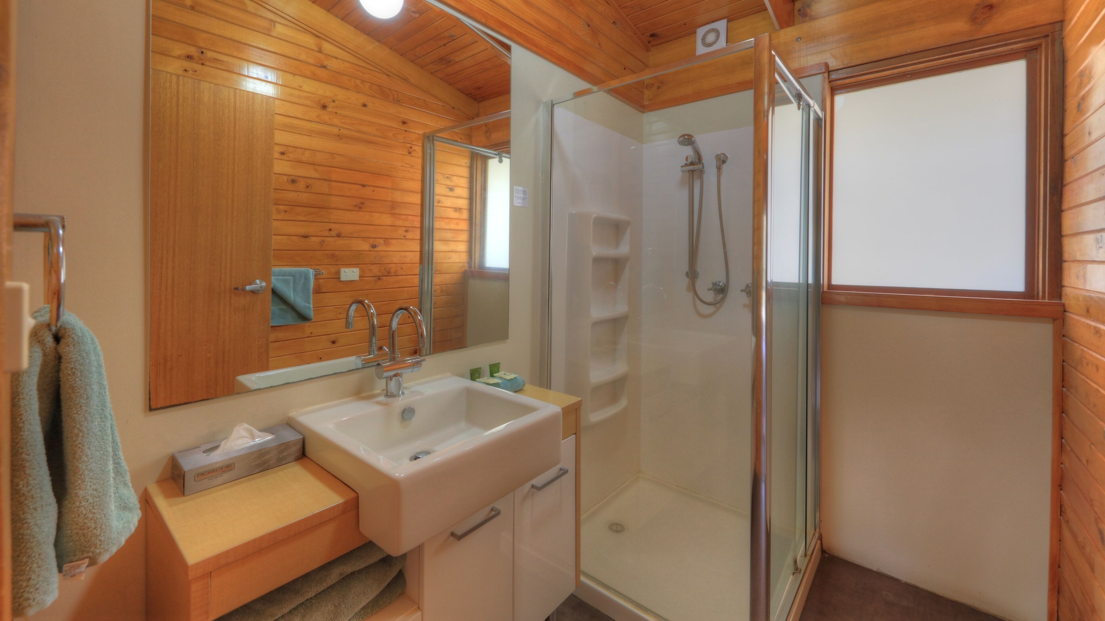 A bathroom with a wooden interior, a sink, a mirror, and a glass-enclosed shower.
