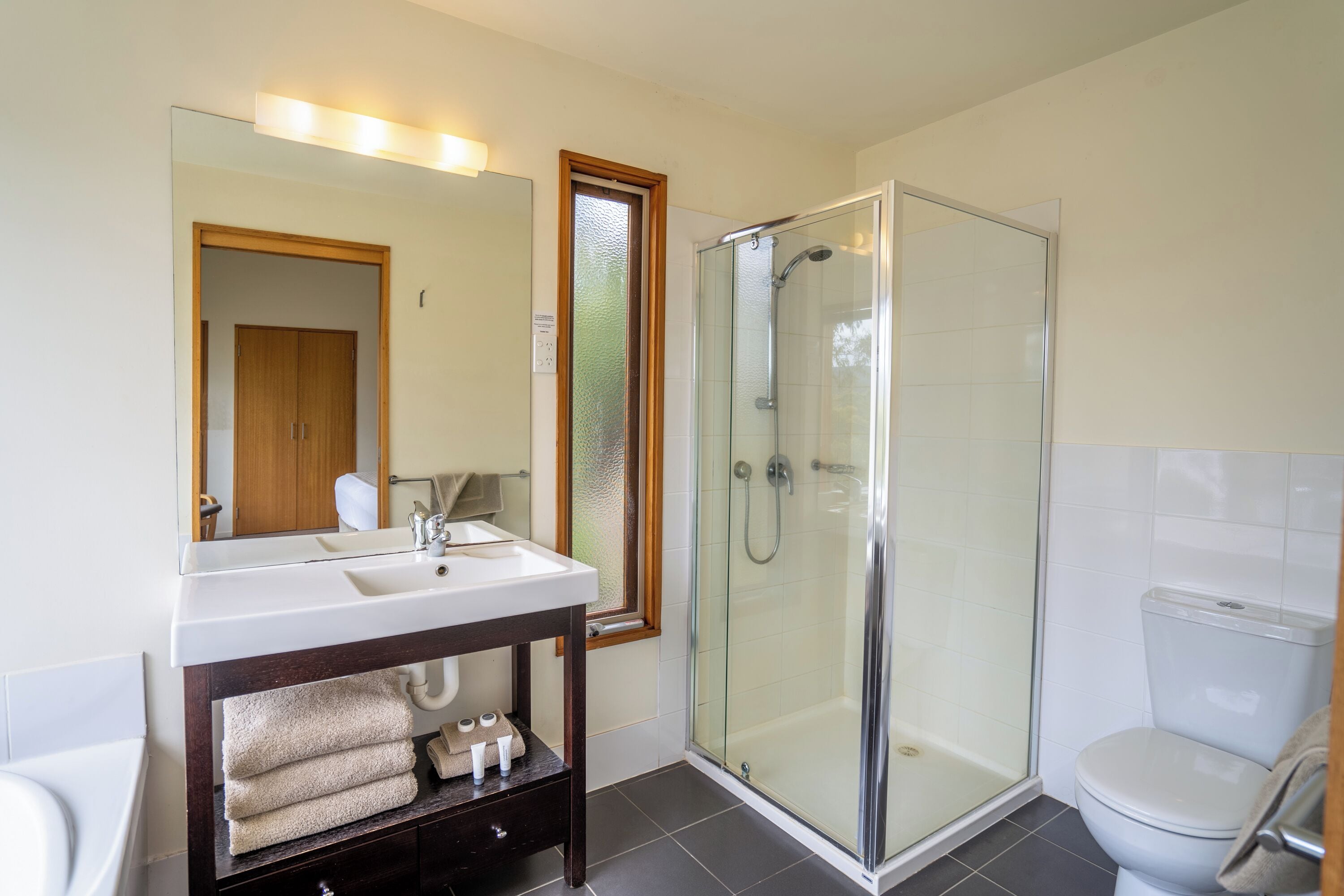 Un baño moderno con ducha envuelta en vidrio, un lavamanos blanco con mueble de madera y un inodoro.