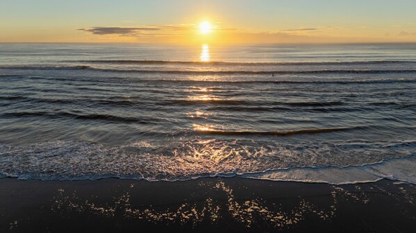 A beach with waves, a sunset, and a clear sky.