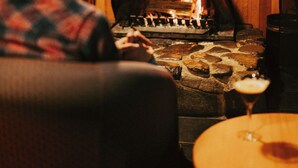 Una persona sentada a una mesa con una chimenea de piedra, un muro de madera y un cuadro colgado sobre la chimenea.
