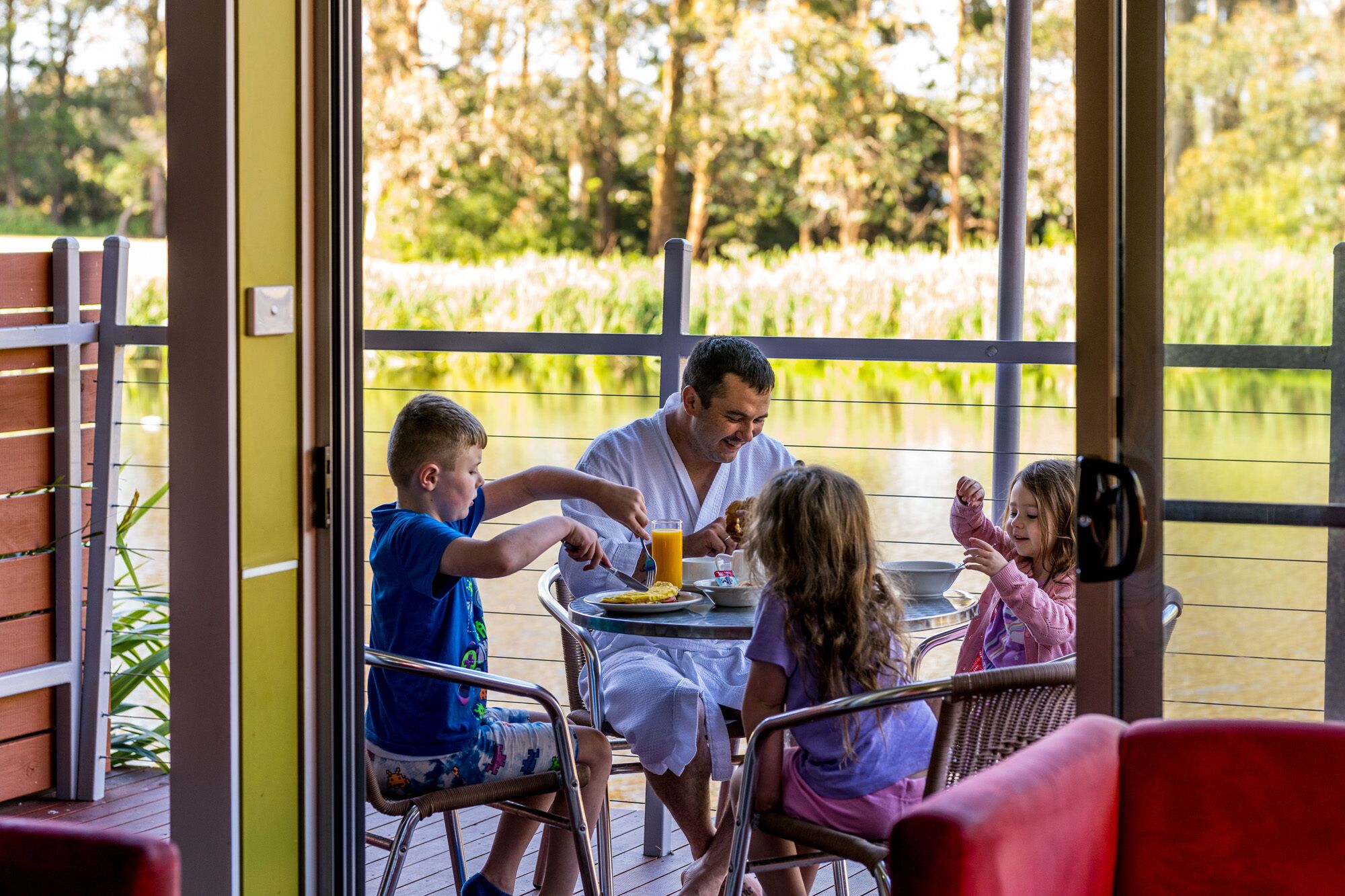 Une famille est assise à une table, près d’un étang, et profite de la vue sur la nature environnante.