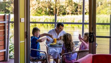 Une famille est assise à une table, près d’un étang, et profite de la vue sur la nature environnante.