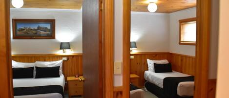 A room with two beds, a wooden headboard, a nightstand with a lamp, and a framed picture on the wall.