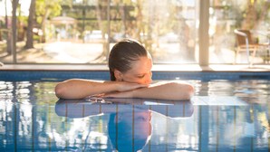 Una persona descansando junto a una piscina con vista a un jardín y un espacio exterior con mobiliario.