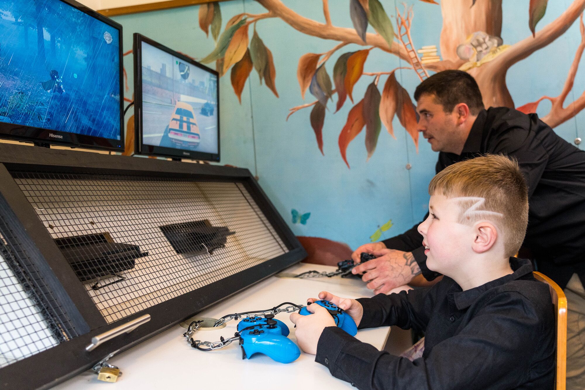 Uma criança jogando videogame em frente a um monitor que exibe um jogo de corrida, um teclado e um mouse sobre uma mesa.