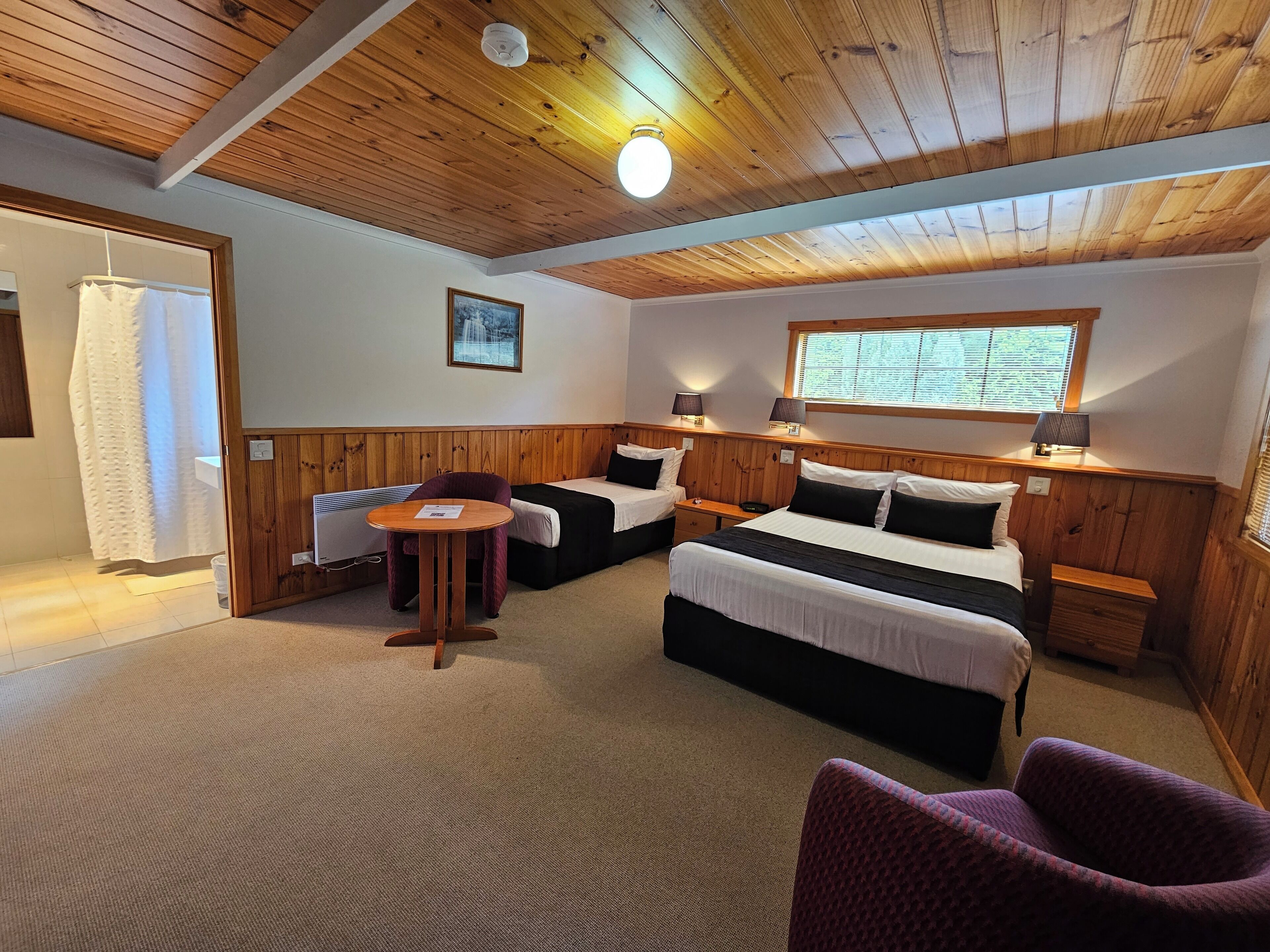 A cozy room with wooden paneling, two beds, a small table, and a window with a view.