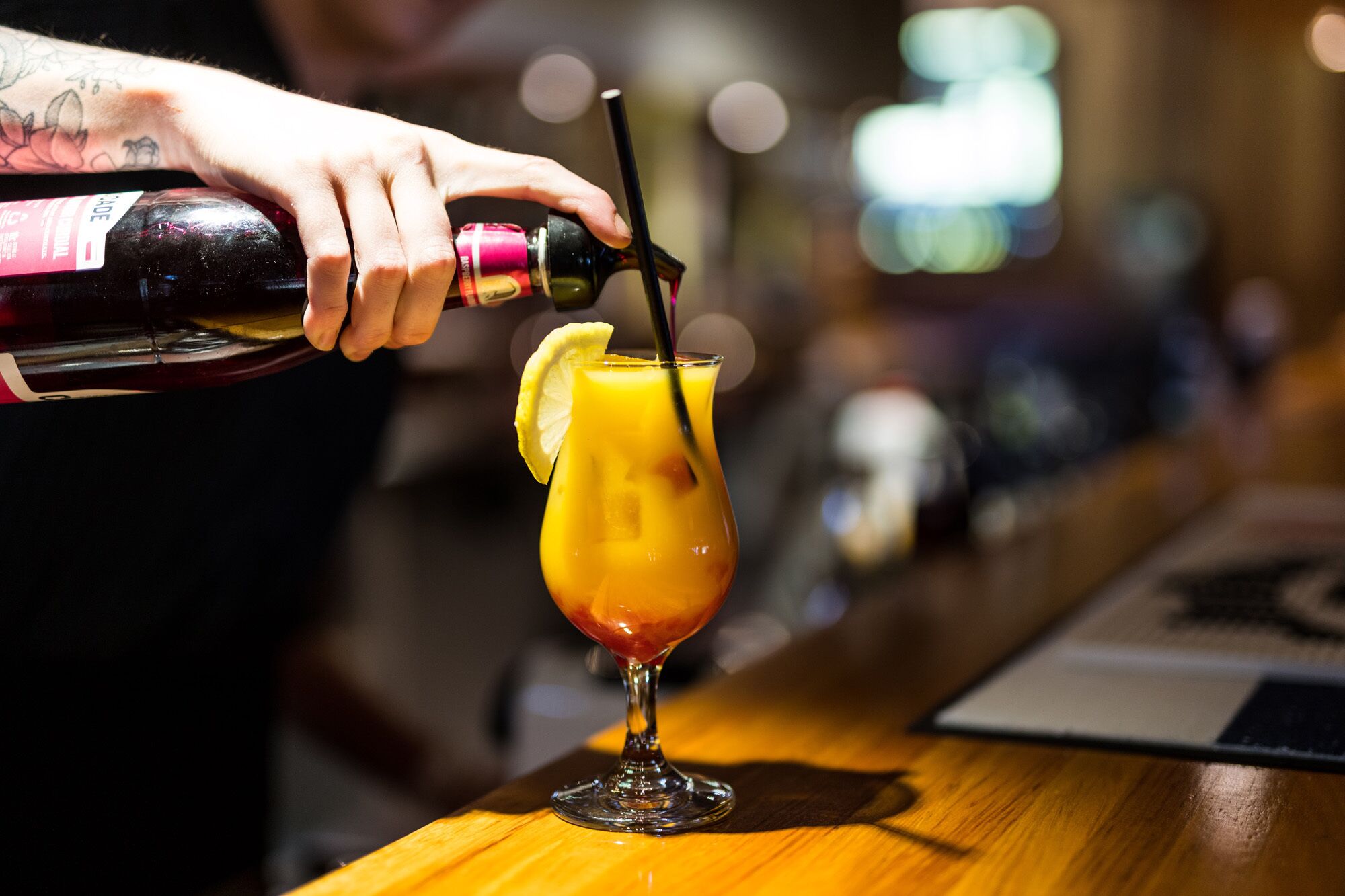 A bartender pouring a drink into a glass with a lemon slice.