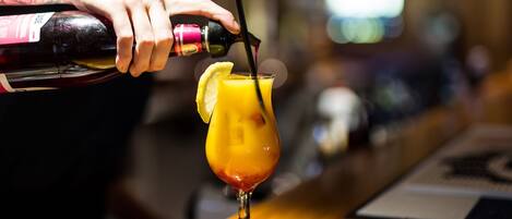A bartender pouring a drink into a glass with a lemon slice.