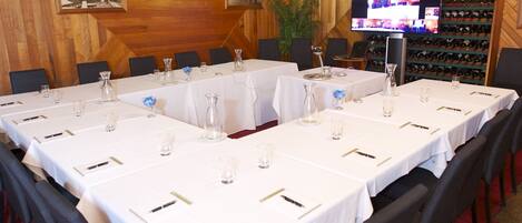 A conference room with long tables set for a meeting, wooden walls, a chandelier, and a wine rack in the background.