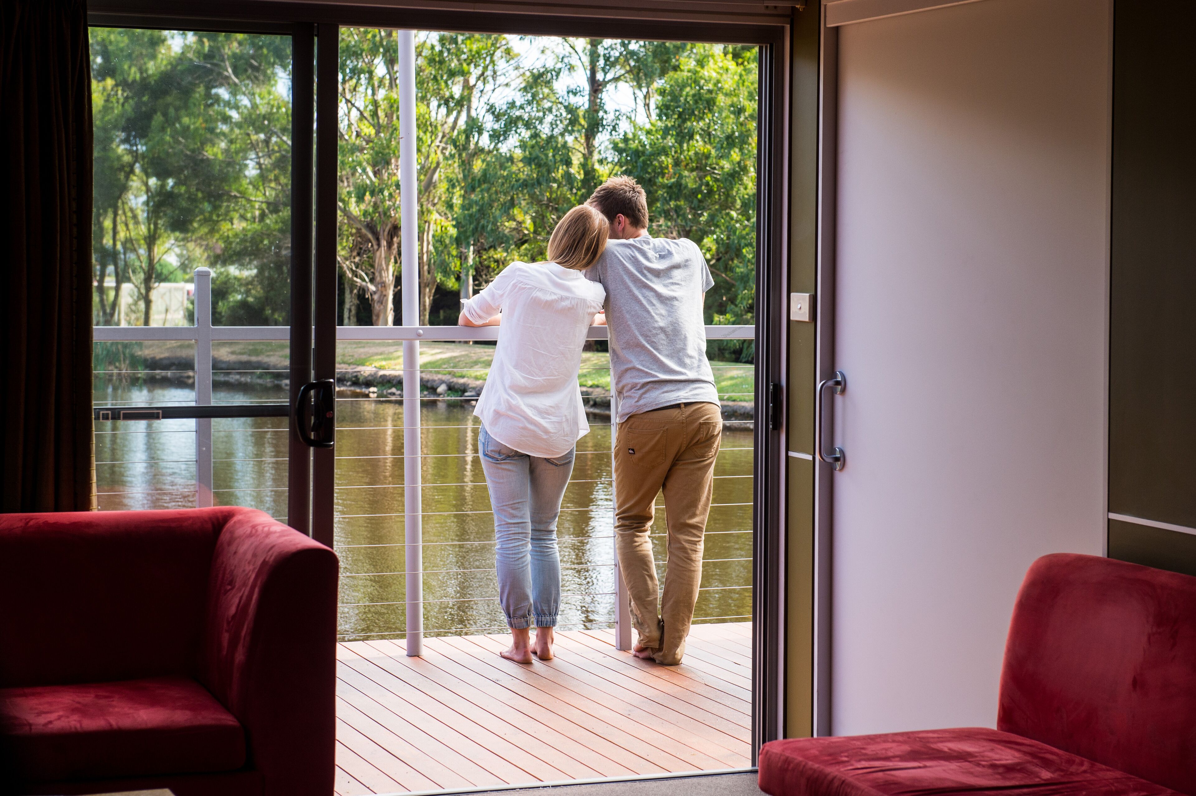 Una pareja está de pie sobre una terraza de madera con un ventanal de vidrio que da a un jardín.