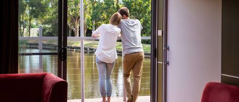 Una pareja está de pie sobre una terraza de madera con un ventanal de vidrio que da a un jardín.