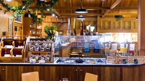 Una barra de restaurante con distintos alimentos y condimentos, mobiliario de madera y plantas colgantes.