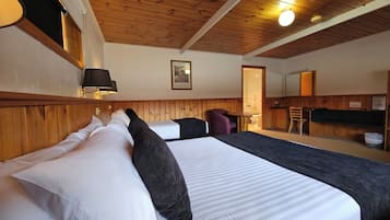 Hotelkamer met houten plafond, een bed met zwart-wit beddengoed, een tafeltje, een stoel en een zichtbare badkamer door een open deur.