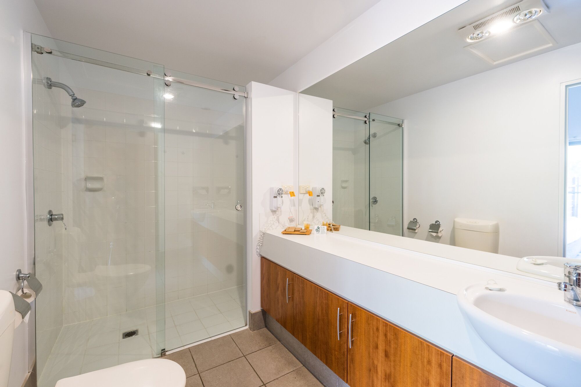A modern bathroom with a glass shower enclosure, a large mirror, and a vanity with a sink.