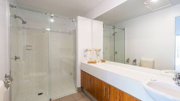 A modern bathroom with a glass shower enclosure, a large mirror, and a vanity with a sink.