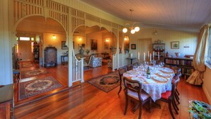 Una àmplia zona de menjador amb un gran tauler de fusta preparat per a dinar, envoltat de cadires. Hi ha una escala que condueix a un nivell superior, i una prestatgeria plena de llibres.