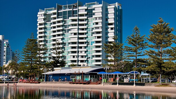 Um hotel moderno com várias varandas, localizado à beira-mar, com o reflexo visível na água.