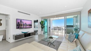 Uma sala de estar moderna com uma televisão de tela plana grande, uma mesa de centro de vidro e um sofá bege.