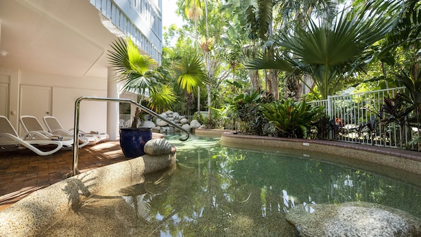 Zona de piscina con sillones, una palmera y un sendero de piedra.