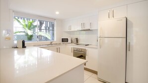 Una cocina moderna con armarios blancos, horno empotrado, microondas y refrigerador.
