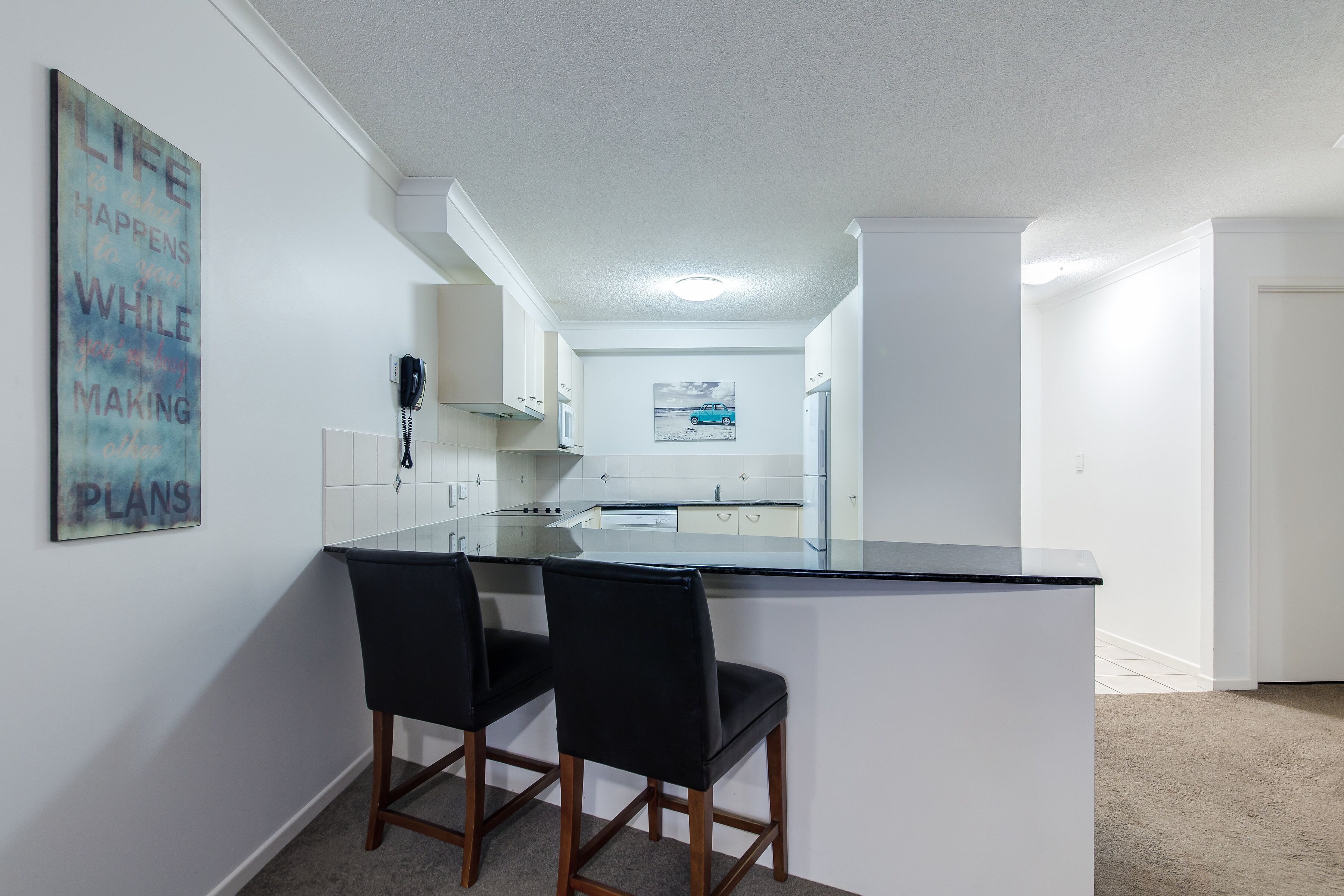 Een moderne keuken met witte kasten, een zwart aanrecht en twee zwarte stoelen.