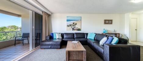 Un salon moderne avec un canapé d’angle, une table basse en bois et une vue sur l’extérieur.