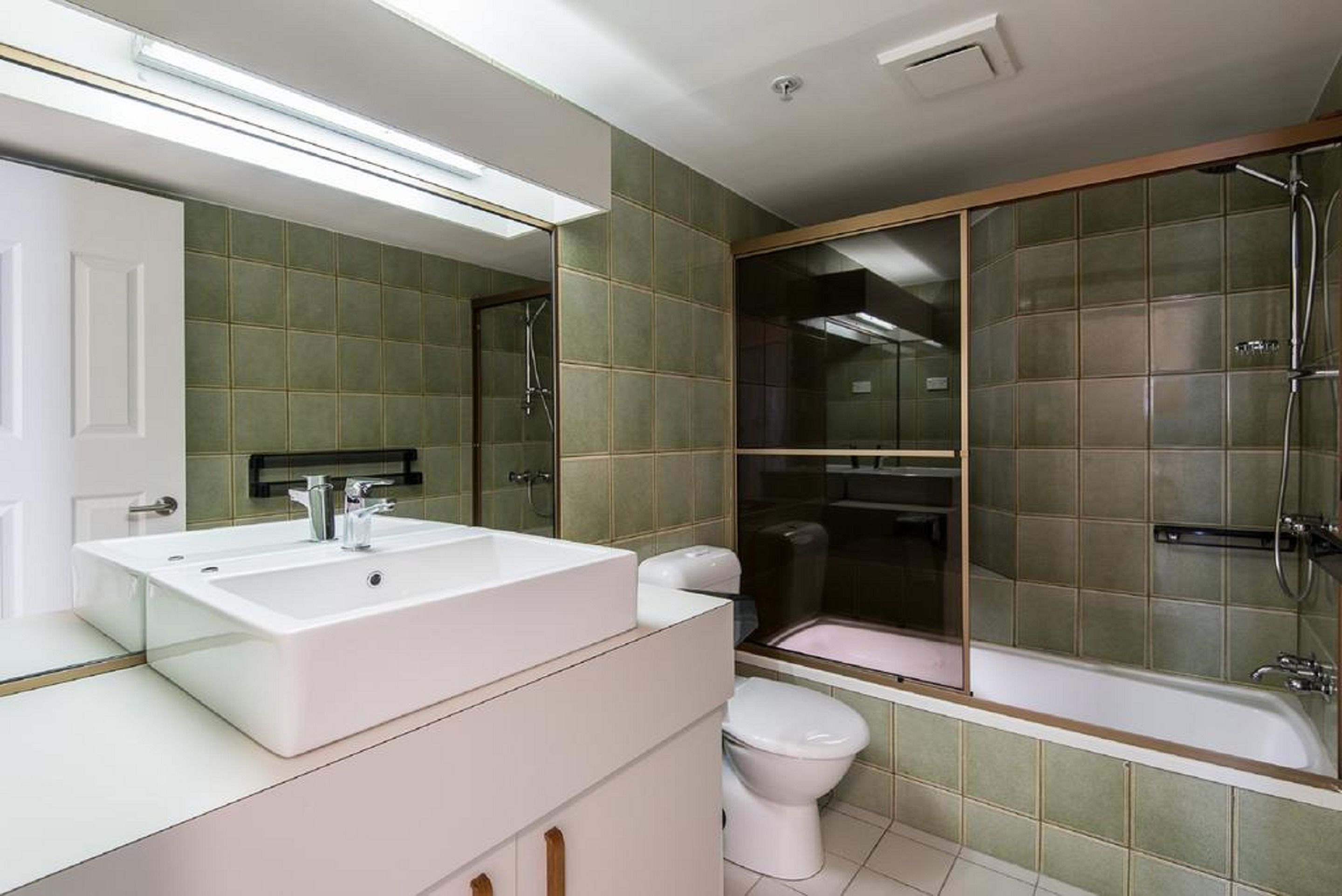Un baño con un lavamanos grande blanco, un inodoro y una zona de ducha con mampara de vidrio.