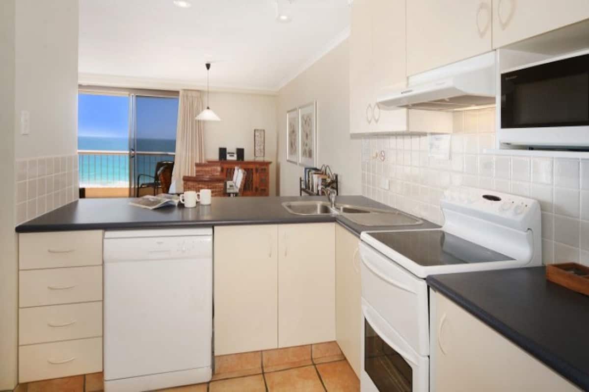 A kitchen with a dishwasher, stove, and microwave. There is a view of the ocean through a window.