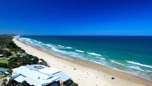 A beach with a clear view of the ocean, a sandy shore, and a few buildings in the background. - Coolum Caprice (Coolum Beach)
