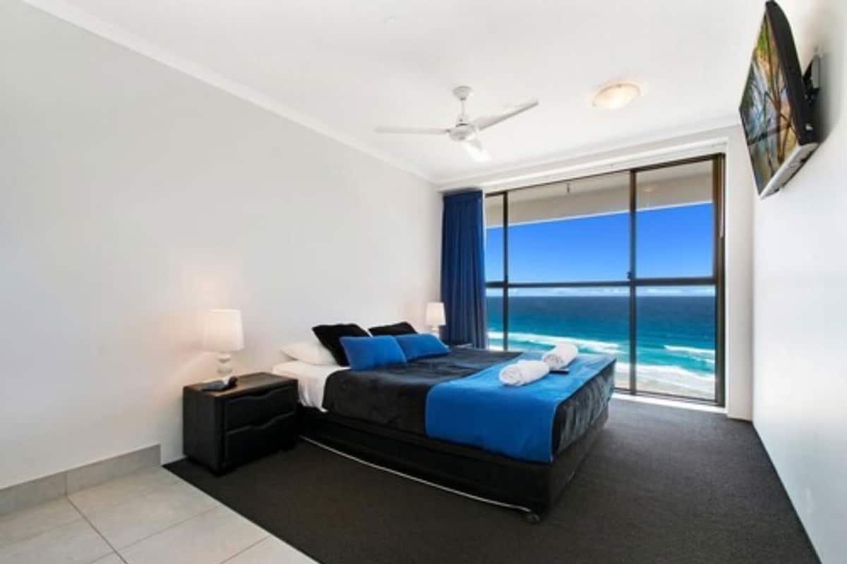 A bedroom with a bed, nightstands, a ceiling fan, and a view of the ocean.