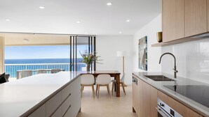A modern kitchen with a large island, wooden cabinets, and a view of the ocean. - Coolum Caprice (Coolum Beach)