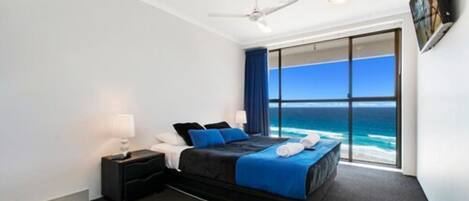 A bedroom with a bed, a nightstand, a ceiling fan, and a large window with a view of the ocean.