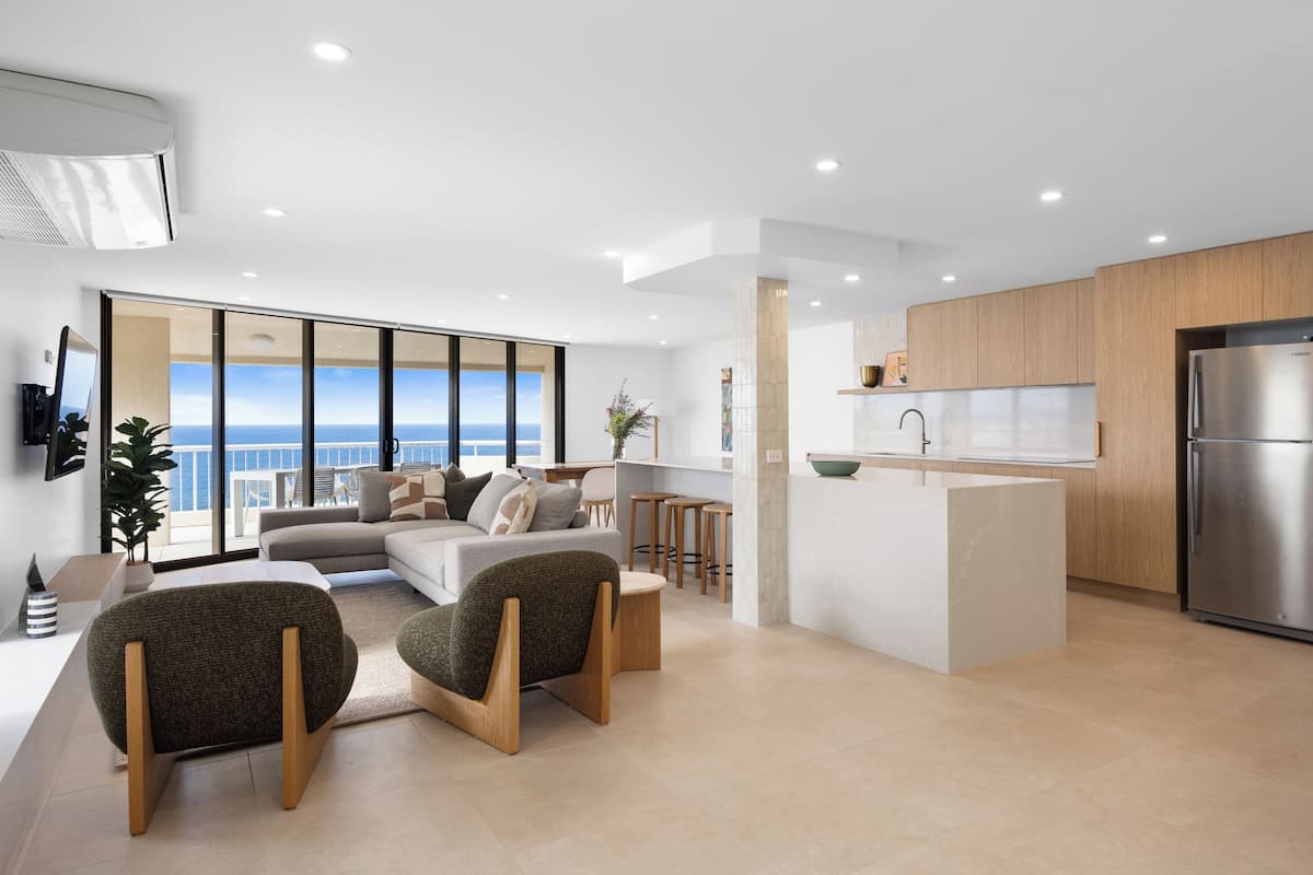 A modern living room with a sofa, two armchairs, a coffee table, and a view of the ocean.