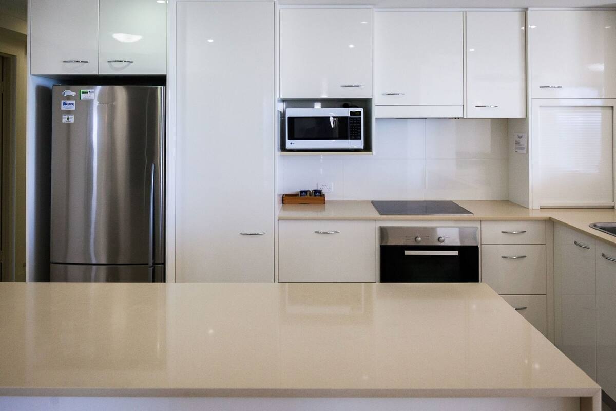 A modern kitchen with stainless steel appliances, white cabinetry, and a beige countertop.