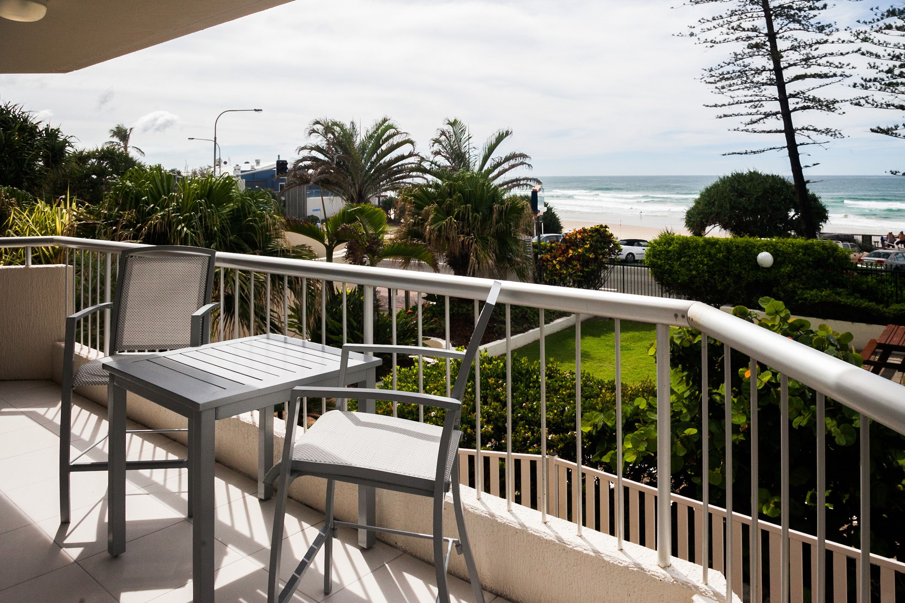 Un balcon avec une table et des chaises, donnant sur une plage et une végétation luxuriante.