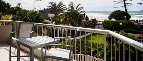 Un balcon avec une table et des chaises, donnant sur une plage et une végétation luxuriante.