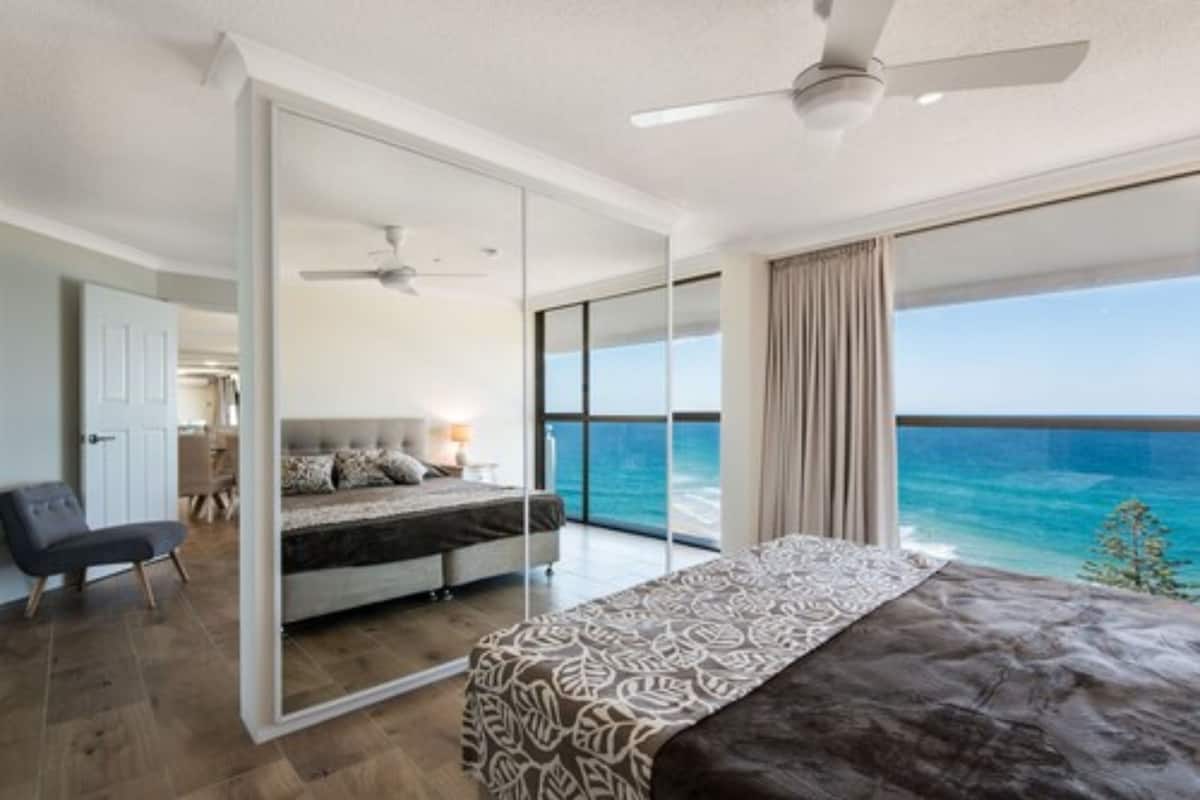 A bedroom with a large bed, a desk, and a view of the ocean.