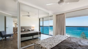 A bedroom with a large bed, a desk, and a view of the ocean. - Coolum Caprice (Coolum Beach)