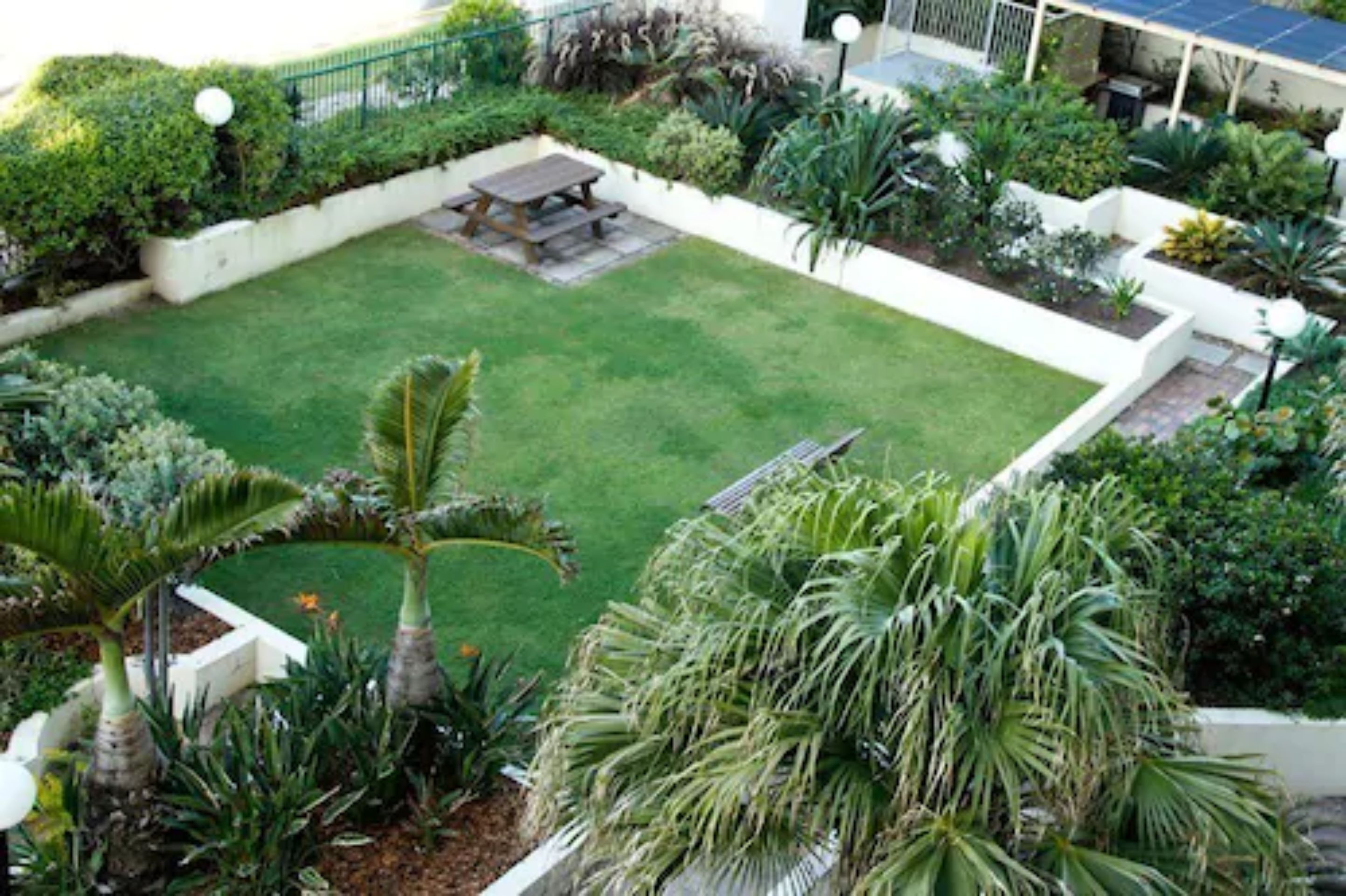 A well-maintained garden with a lawn, palm trees, and a picnic table.